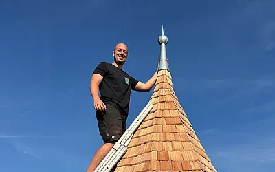 Mitarbeiter steht mit einer Leiter auf der fertig sanierten Turmspitze