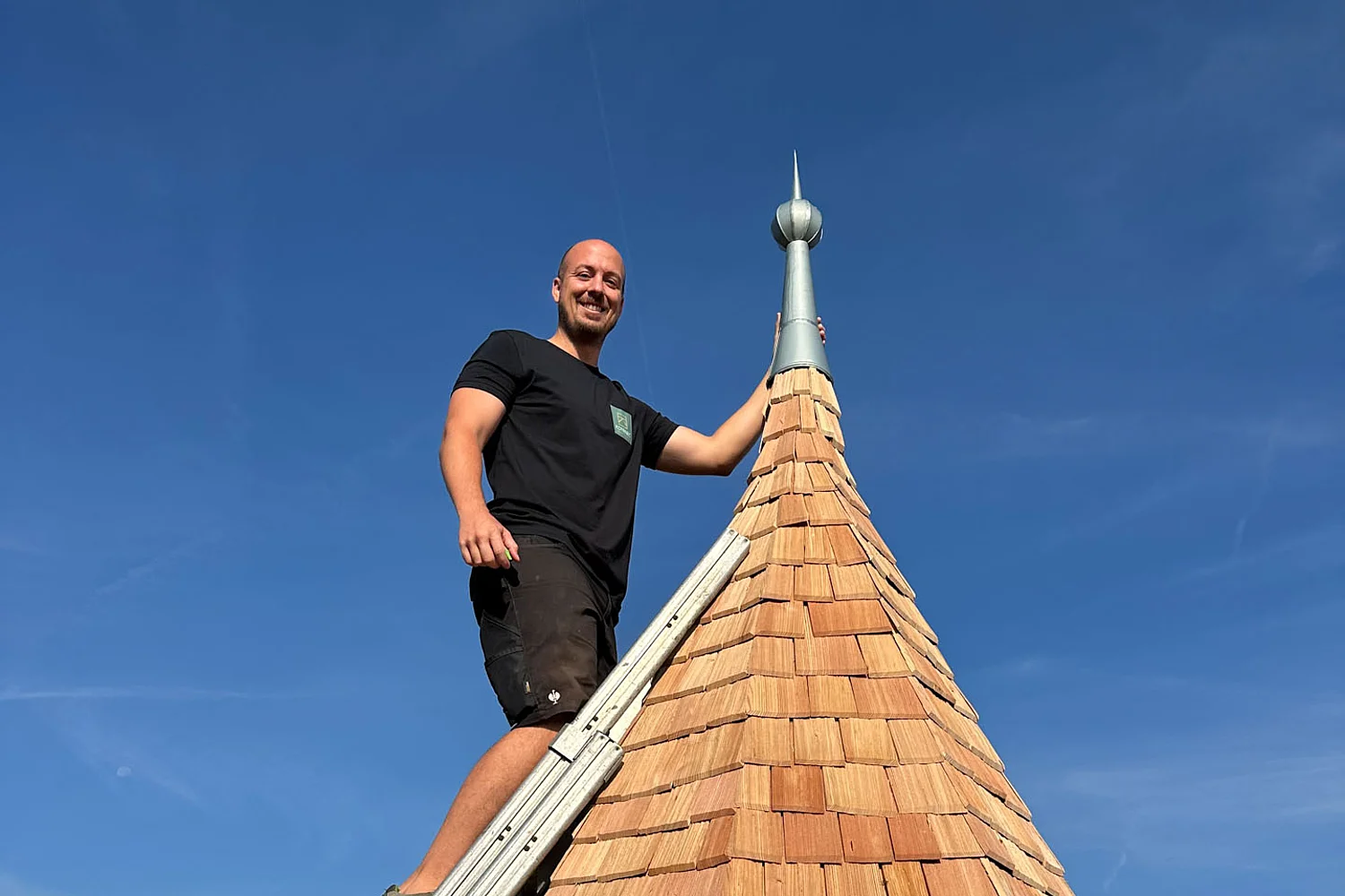 Mitarbeiter steht mit einer Leiter auf der fertig sanierten Turmspitze