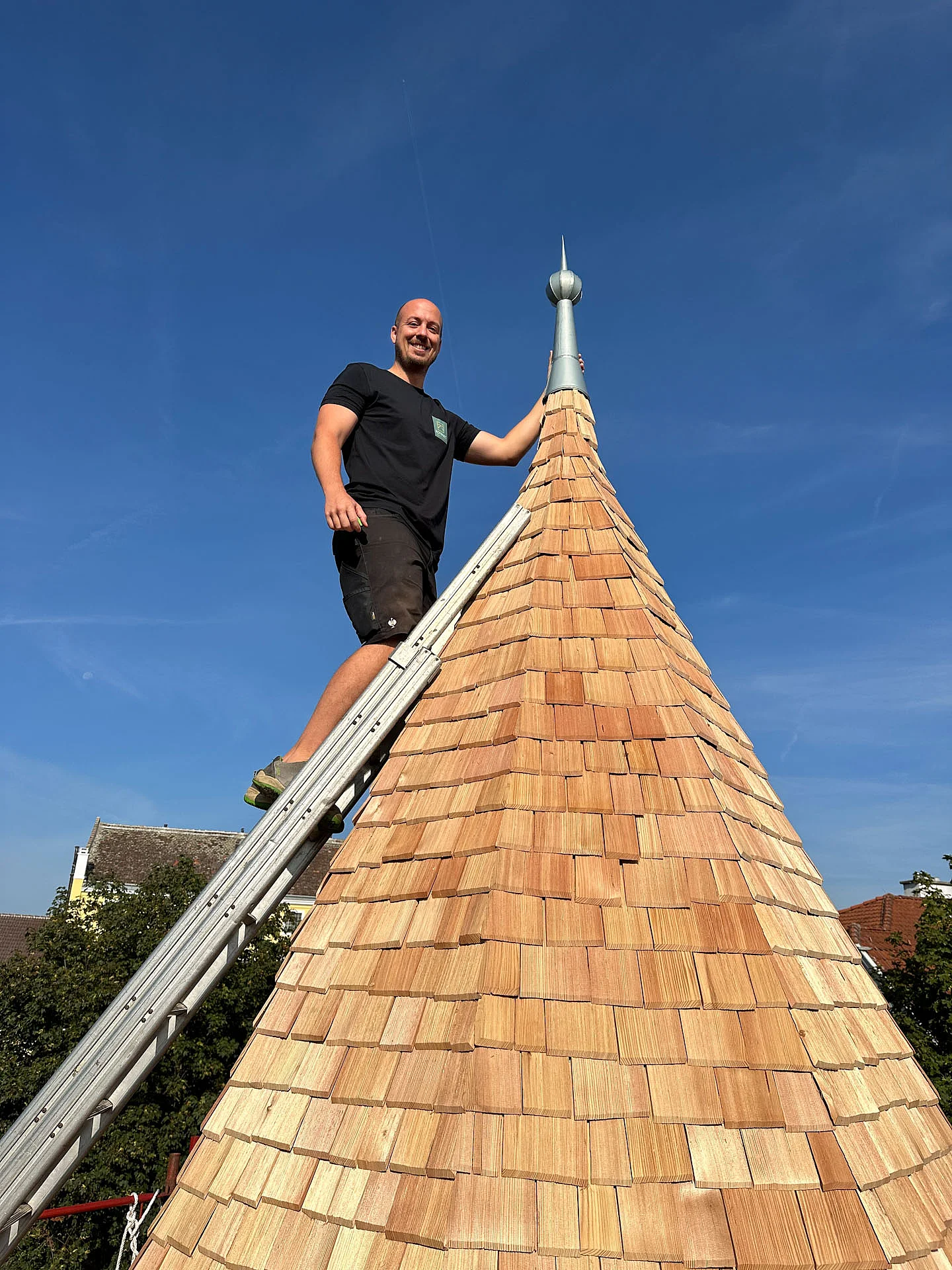 Mitarbeiter steht mit einer Leiter auf der fertig sanierten Turmspitze