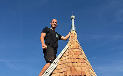 Mitarbeiter steht mit einer Leiter auf der fertig sanierten Turmspitze